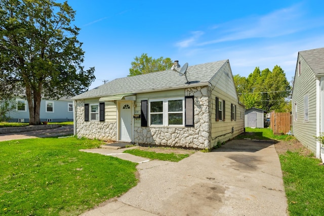 bungalow with stone siding, a storage shed, a shingled roof, an outbuilding, and driveway