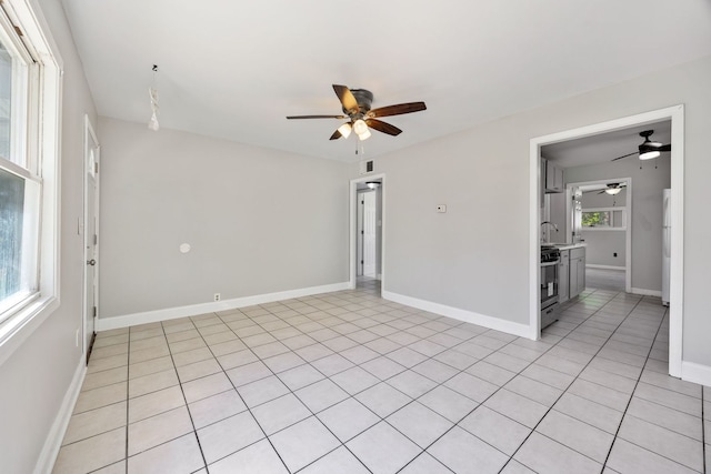 empty room featuring a ceiling fan, baseboards, a sink, and light tile patterned floors