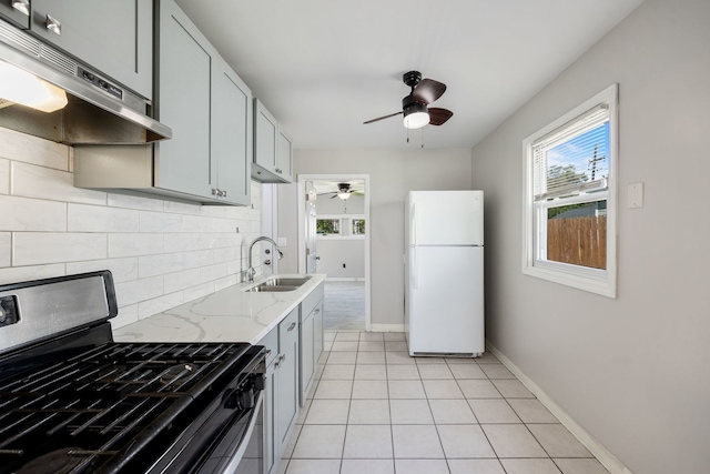 kitchen featuring freestanding refrigerator, stainless steel gas range, a sink, under cabinet range hood, and a ceiling fan