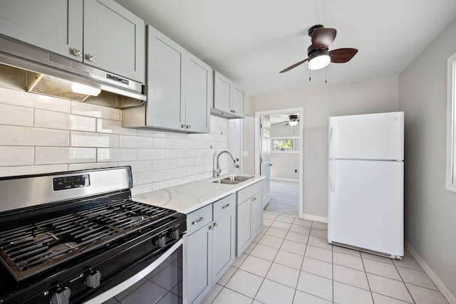 kitchen with freestanding refrigerator, gas range, a sink, ceiling fan, and under cabinet range hood