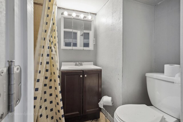 full bath featuring toilet, vanity, a textured wall, and a shower with shower curtain