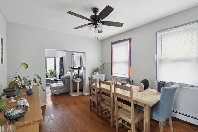 dining area featuring a baseboard heating unit, a ceiling fan, wood finished floors, and baseboards