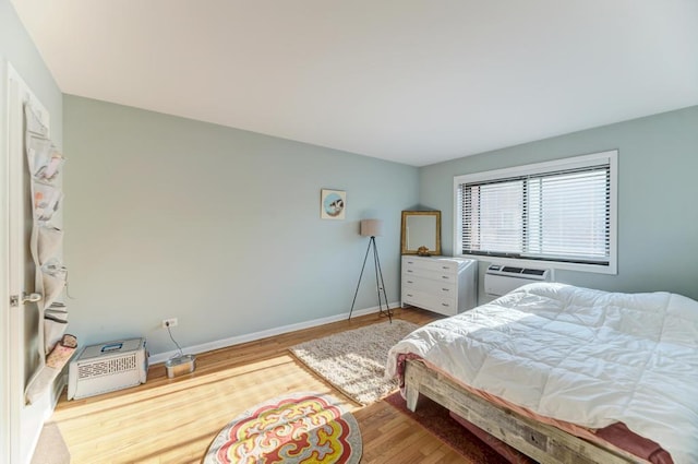 bedroom with an AC wall unit, wood finished floors, and baseboards