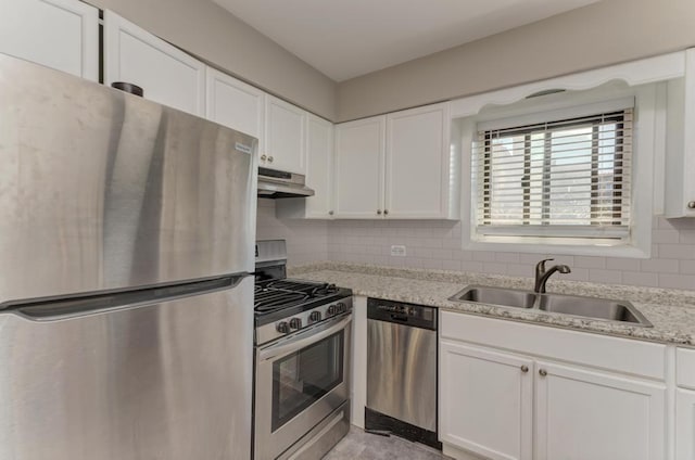 kitchen with appliances with stainless steel finishes, under cabinet range hood, a sink, white cabinets, and tasteful backsplash