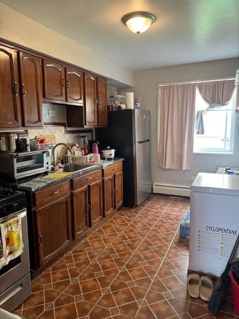kitchen featuring a baseboard heating unit, a sink, gas stove, decorative backsplash, and dark tile patterned floors