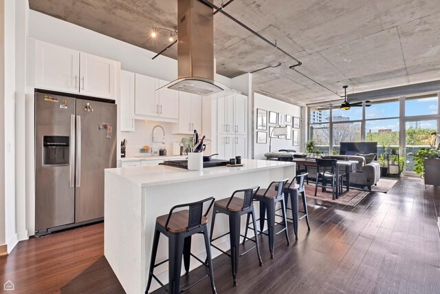 kitchen with stainless steel fridge, island exhaust hood, gas stovetop, dark wood-type flooring, and white cabinetry