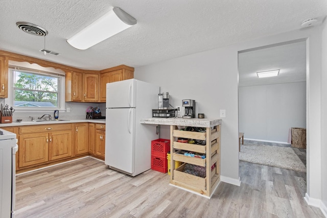 kitchen featuring freestanding refrigerator, light wood finished floors, a sink, a textured ceiling, and light countertops