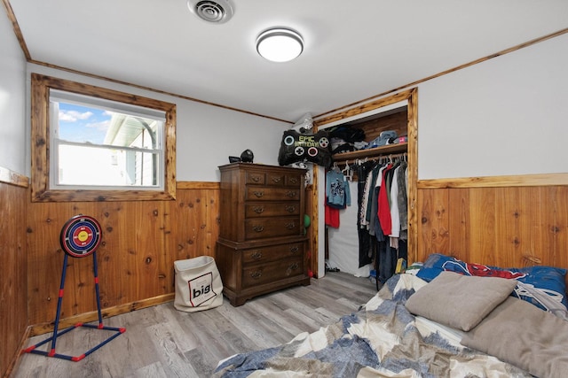 bedroom featuring a wainscoted wall, ornamental molding, a closet, wood walls, and wood finished floors
