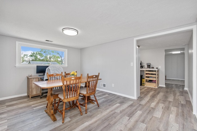 dining space with light wood-style floors, baseboards, and a textured ceiling