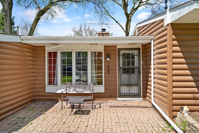doorway to property with a patio, a chimney, and faux log siding
