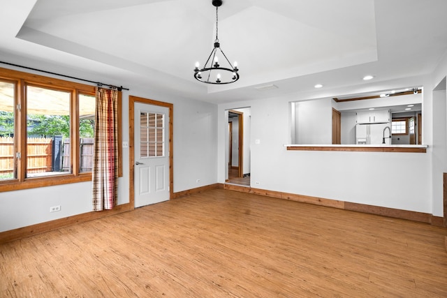 unfurnished living room featuring baseboards, a chandelier, light wood-type flooring, recessed lighting, and a raised ceiling