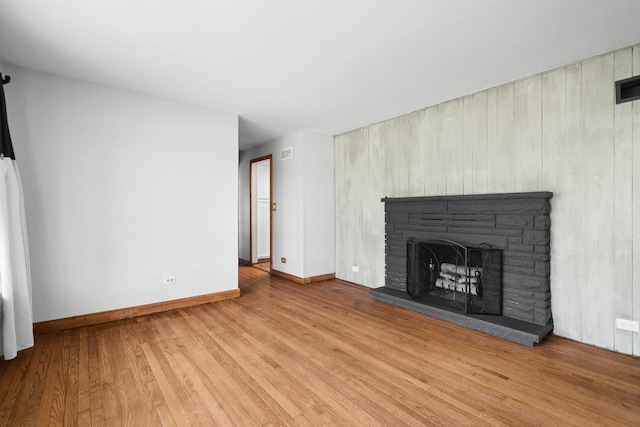 unfurnished living room featuring wood finished floors, a fireplace with raised hearth, and baseboards