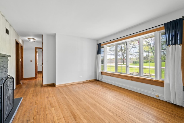 unfurnished living room featuring light wood-type flooring, baseboards, and a fireplace with raised hearth