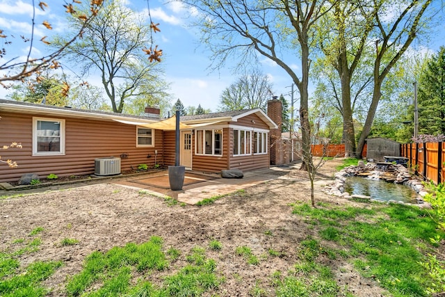 back of property featuring a chimney, a patio area, a fenced backyard, central AC, and faux log siding