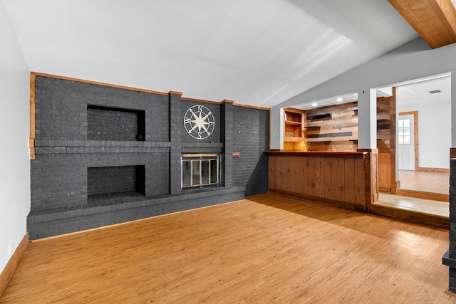 unfurnished living room featuring a brick fireplace, wood finished floors, lofted ceiling, and baseboards