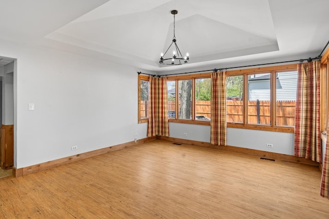 unfurnished room with a raised ceiling, a chandelier, light wood-style floors, and baseboards