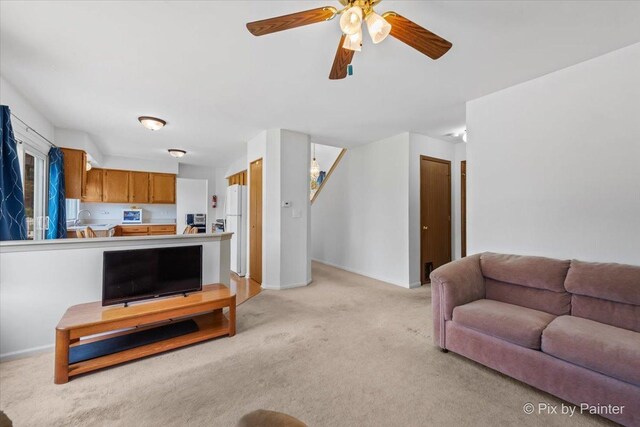 living room featuring light colored carpet, baseboards, and a ceiling fan