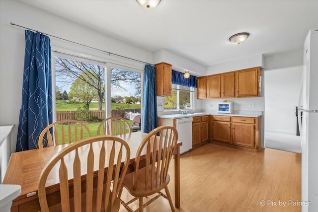 kitchen featuring light countertops, white appliances, light wood-style floors, brown cabinets, and a sink