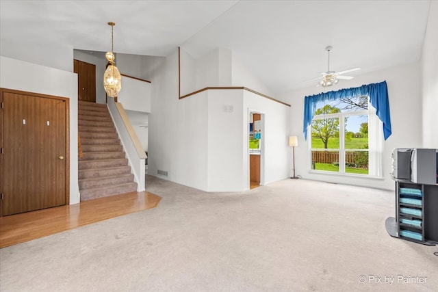 unfurnished living room featuring carpet flooring, stairway, ceiling fan, and high vaulted ceiling