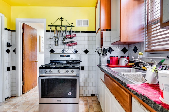 9245 S Justine St, Chicago, IL 60620 - kitchen with stainless steel range with gas stovetop, a sink, white cabinetry, dark countertops, and tasteful backsplash