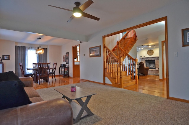 living area with stairs, baseboards, a ceiling fan, carpet floors, and a brick fireplace