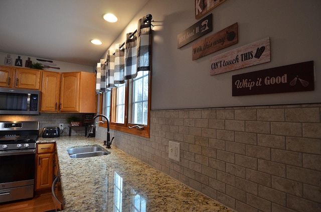 kitchen featuring appliances with stainless steel finishes, a sink, light stone countertops, backsplash, and recessed lighting