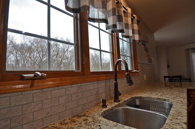 kitchen featuring a sink, decorative backsplash, light stone counters, and vaulted ceiling