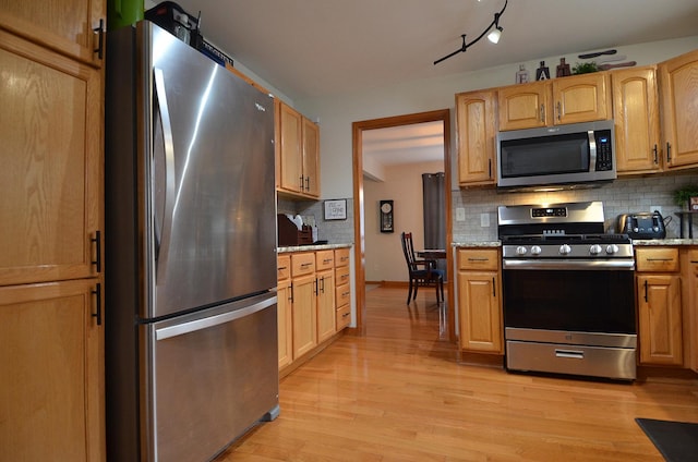 kitchen with appliances with stainless steel finishes, backsplash, light wood-style flooring, and light stone countertops