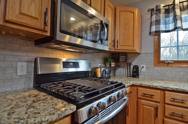 kitchen with appliances with stainless steel finishes, tasteful backsplash, light stone countertops, and brown cabinetry
