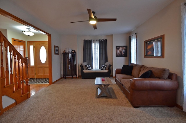 living area featuring light colored carpet, stairway, a ceiling fan, and baseboards