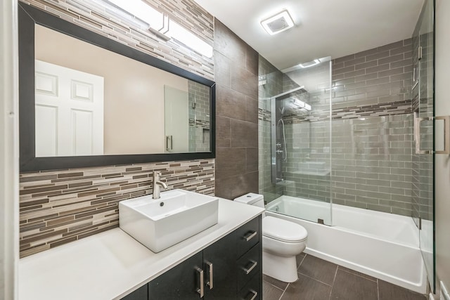 bathroom featuring tasteful backsplash, toilet, combined bath / shower with glass door, vanity, and tile patterned flooring