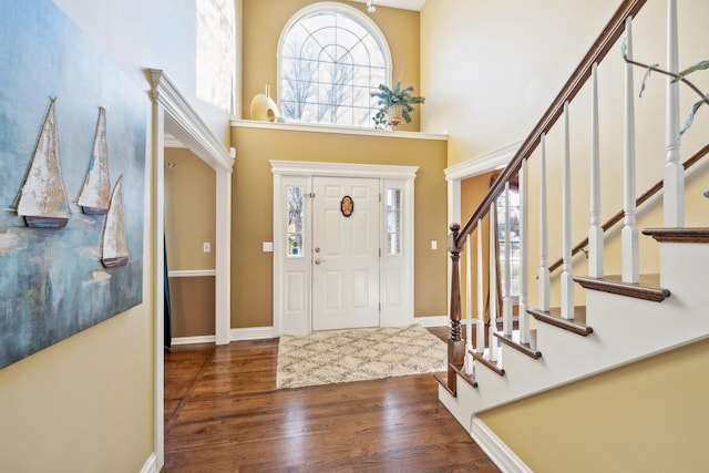 foyer with a towering ceiling, wood finished floors, stairway, and baseboards