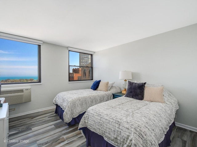 bedroom featuring wood finished floors, baseboards, and an AC wall unit