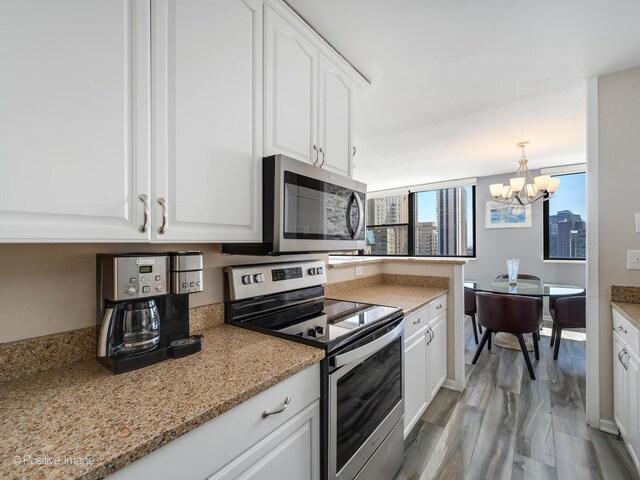 kitchen featuring appliances with stainless steel finishes, a chandelier, white cabinetry, wood finished floors, and light stone countertops