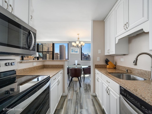 kitchen featuring stainless steel appliances, a sink, a chandelier, light wood-type flooring, and white cabinetry