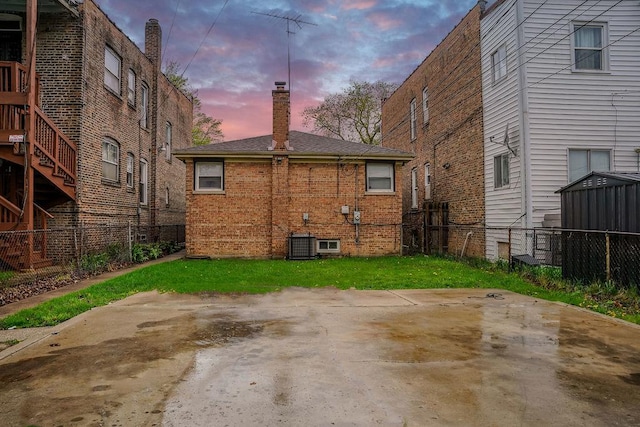 9539 S Forest Ave, Chicago, IL 60628 - back of house at dusk with a chimney, brick siding, a patio area, fence, and central AC