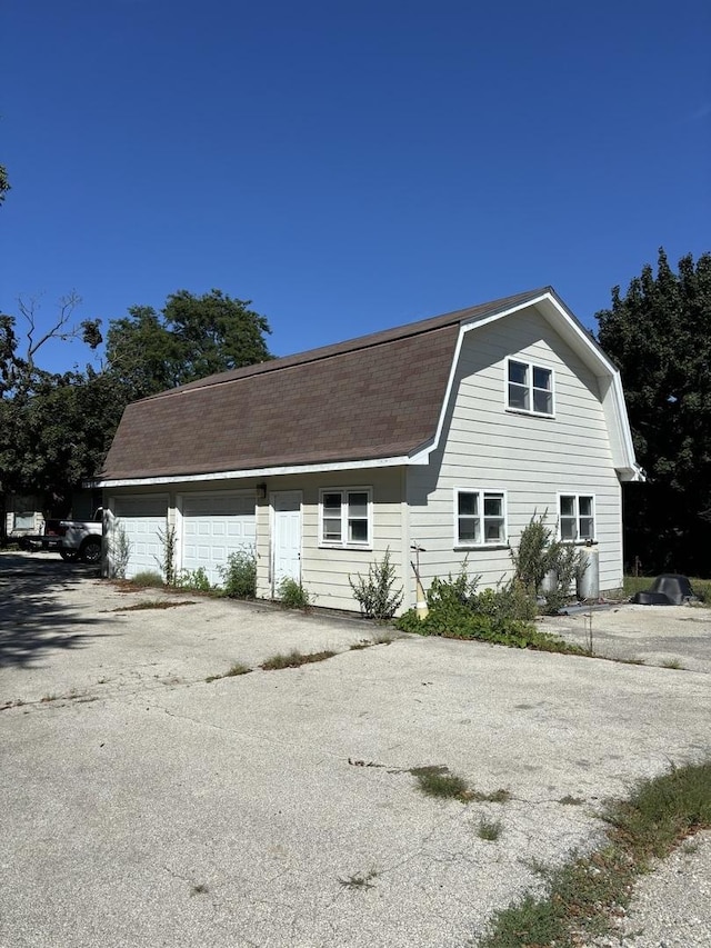 view of side of property featuring a gambrel roof, roof with shingles, and a garage