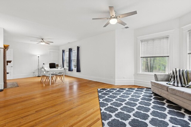 living room featuring ceiling fan, baseboards, and light wood-style flooring