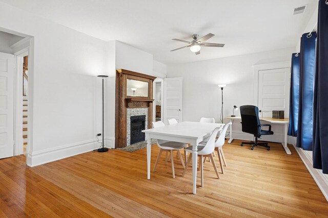 dining space with a fireplace, ceiling fan, light wood finished floors, baseboards, and an office area
