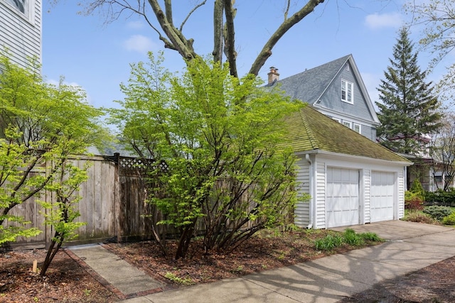 view of side of home featuring fence, a chimney, a shingled roof, and a garage