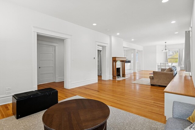 living room featuring light wood-type flooring, recessed lighting, baseboards, a chandelier, and a fireplace with flush hearth