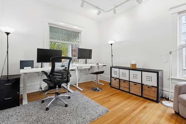 office space featuring rail lighting, hardwood / wood-style flooring, plenty of natural light, and baseboards