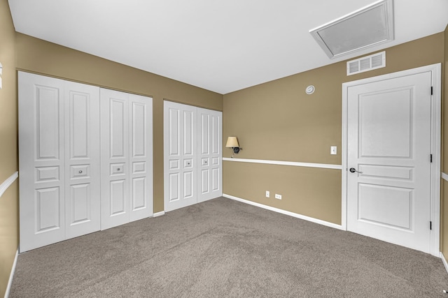 unfurnished bedroom featuring multiple closets, carpet flooring, baseboards, and attic access