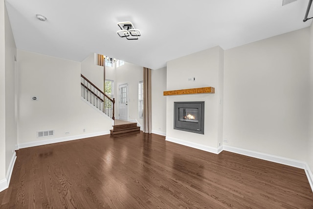 unfurnished living room featuring stairs, wood finished floors, baseboards, and a glass covered fireplace