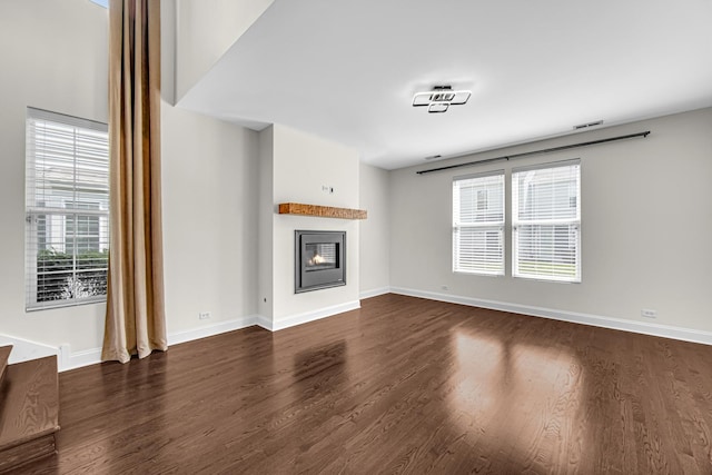 unfurnished living room with dark wood-type flooring, plenty of natural light, a glass covered fireplace, and baseboards