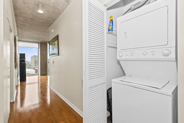 washroom featuring stacked washer / dryer, wood finished floors, and baseboards