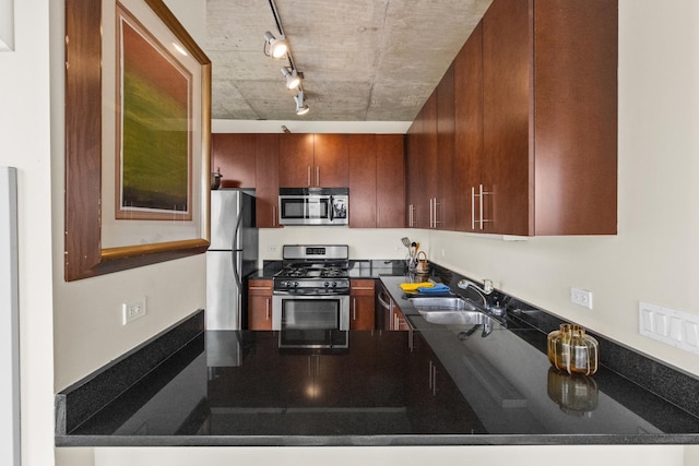 kitchen with appliances with stainless steel finishes, a sink, track lighting, dark countertops, and a peninsula