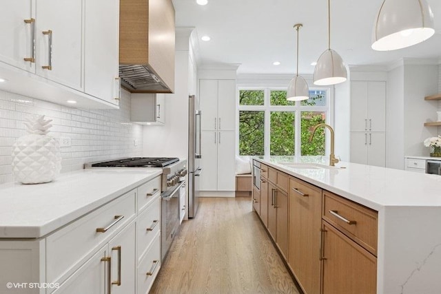 kitchen with a sink, wall chimney range hood, high end appliances, light wood finished floors, and light countertops