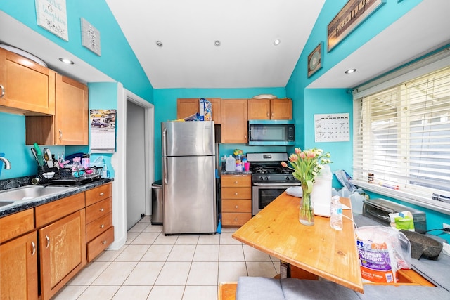 kitchen featuring appliances with stainless steel finishes, a sink, light tile patterned flooring, dark countertops, and lofted ceiling