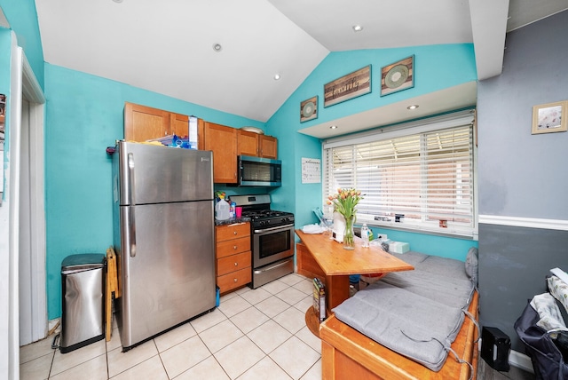 kitchen with appliances with stainless steel finishes, lofted ceiling, light tile patterned floors, and brown cabinets